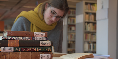 Foto: Eine Studentin sitzt in der Bibliothek und liest ein Buch. Vor ihr liegt ein Stapel aus mehreren Büchern der Iranistik.